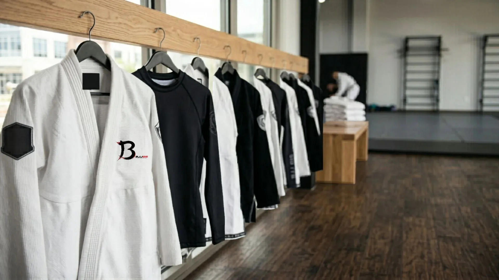 White gis and black rash guards with BJJ Gis logo on a clothing rack