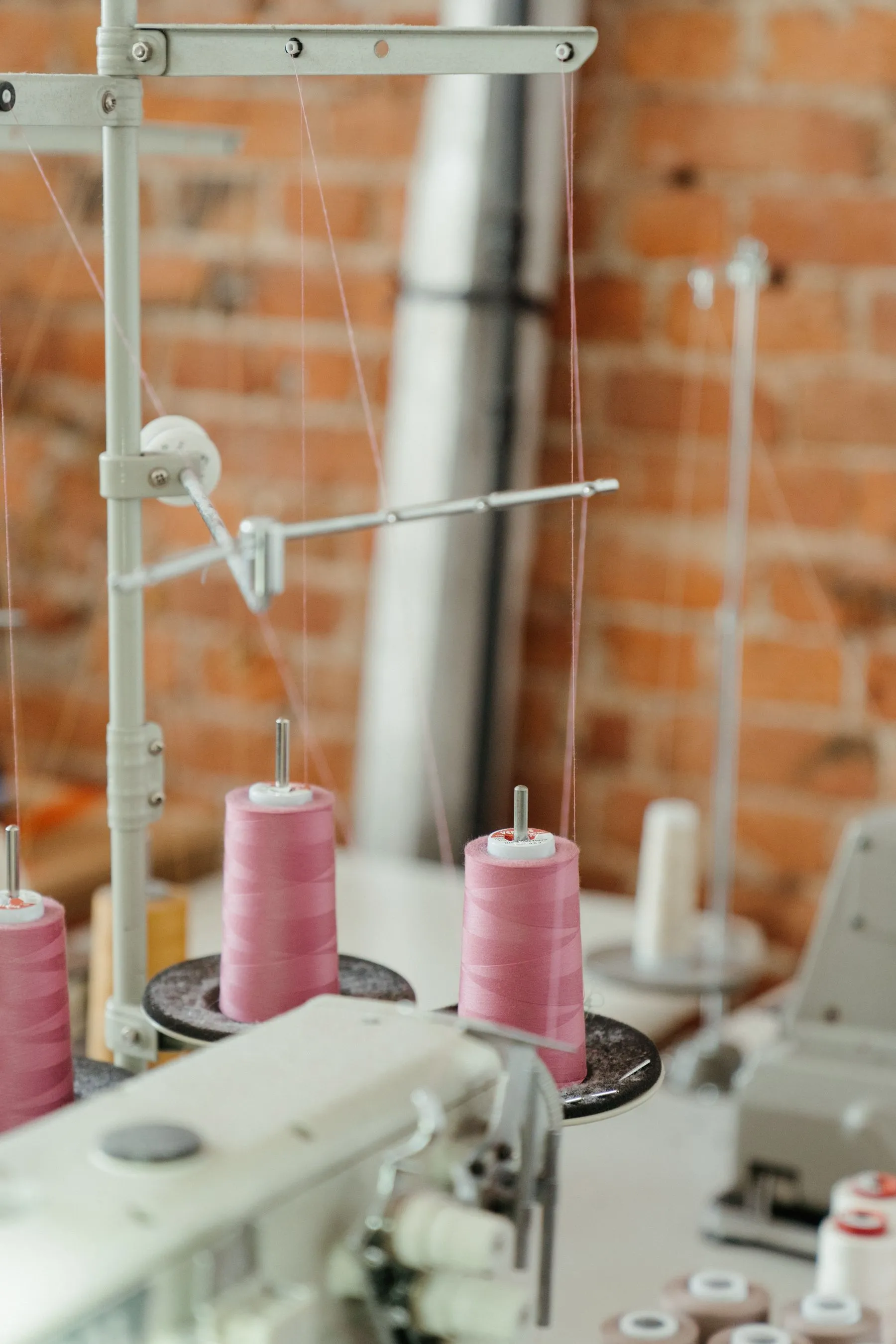 Pink thread cones on an industrial sewing machine stand against a brick wall