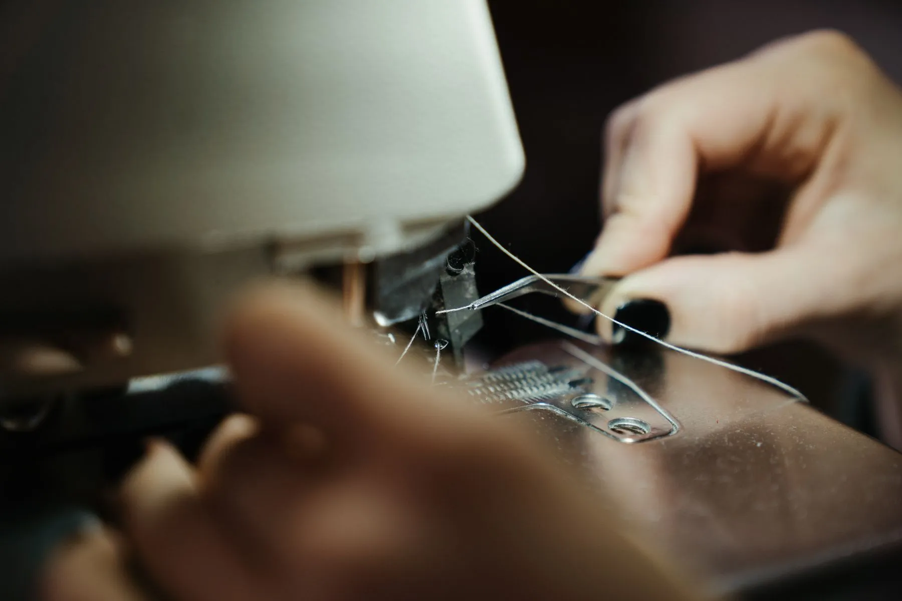 Hands threading an industrial sewing machine